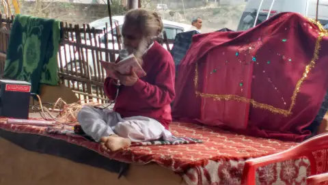 Nepali Baba seated beside the decorated shrine during worship